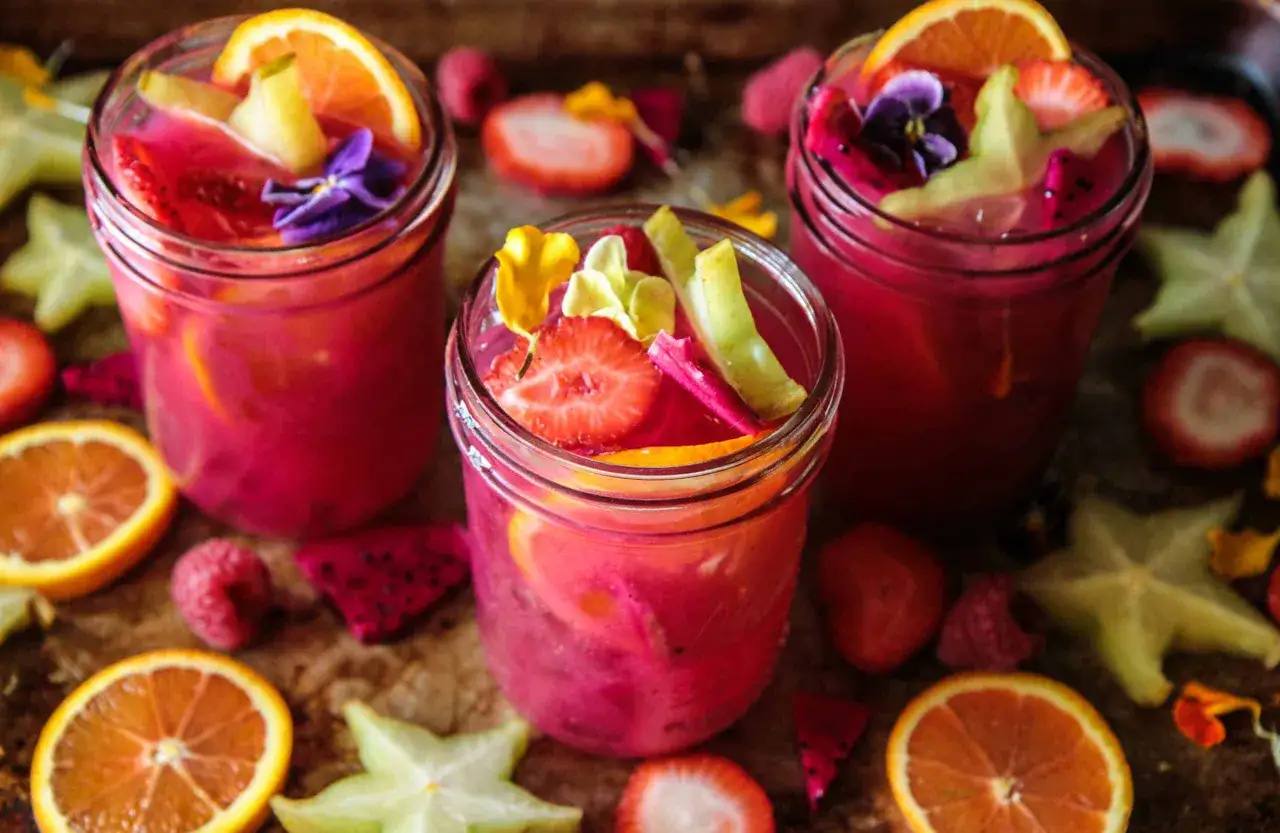 Trois verres remplis d'un punch fruit&eacute; rose vif, garni de fraises, d'oranges et de fleurs comestibles. Une recette punch simple pour l'&eacute;t&eacute;.