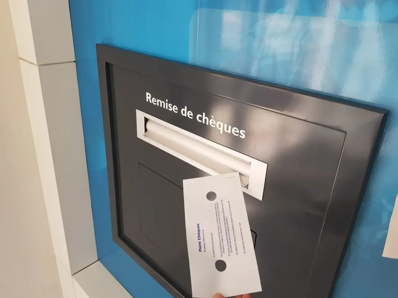 Une main tient une enveloppe pour un dépôt de chèques dans une fente murale.
