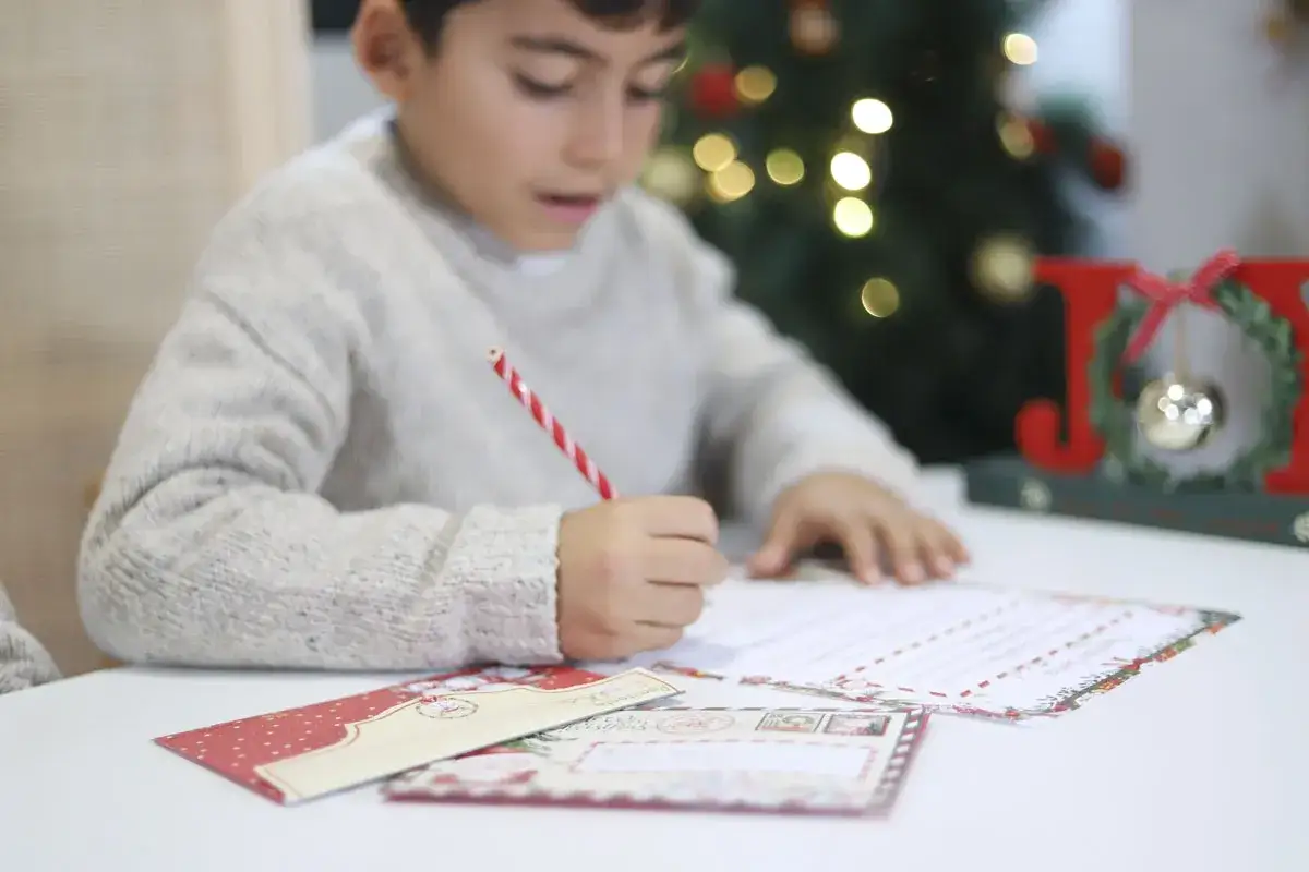 Niño concentrado escribiendo su carta para escribir a Papá Noel, con un árbol de Navidad y decoración de