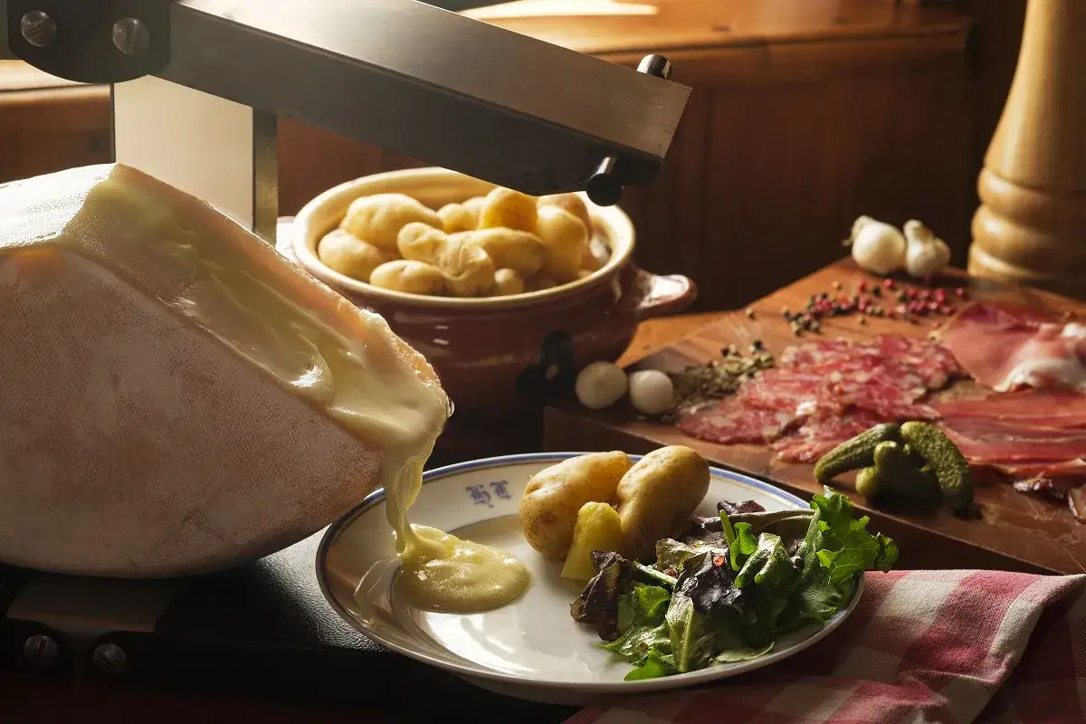 Fromage fondant coulant sur une assiette avec pommes de terre et salade, accompagnés de charcuterie. Une raclette classique réconfortante.