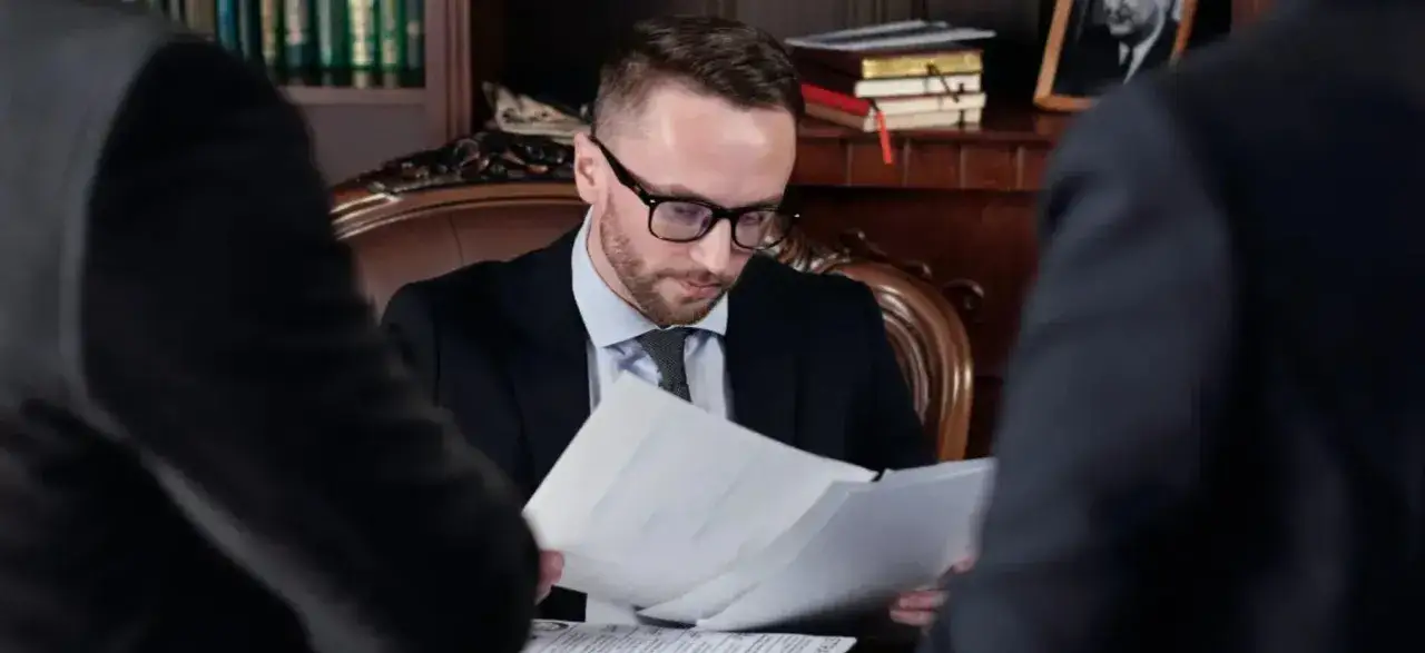 Prawnik w okularach analizuje dokumenty, omawiając z klientami, jak wygląda spłata spadku.