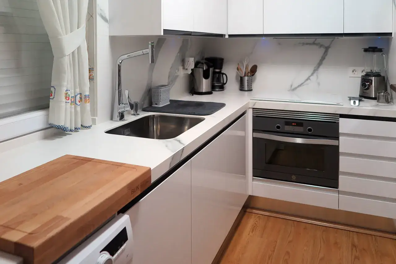 Cocina moderna y funcional, lista para reformar. Encimera blanca, fregadero, horno y electrodom&eacute;sticos.