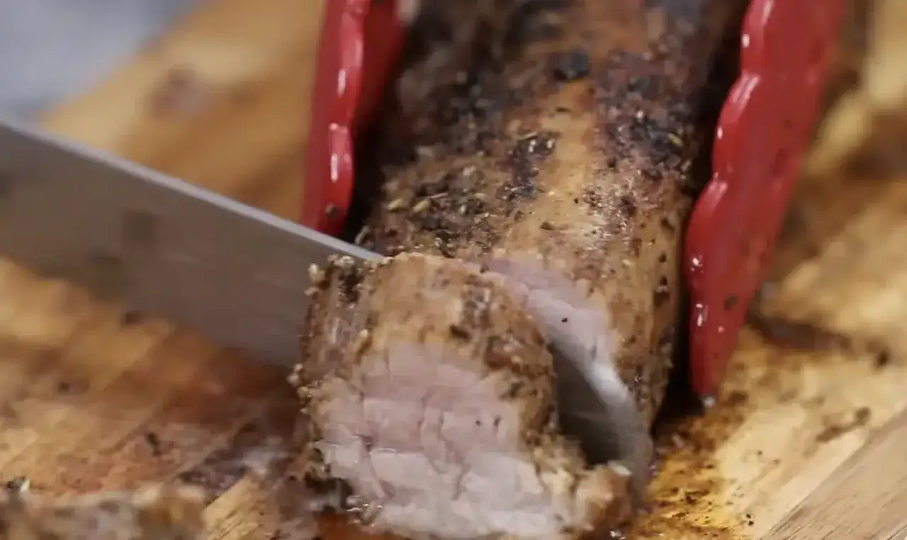 Un jugoso solomillo de cerdo al horno, reci&eacute;n cortado en una tabla de madera.