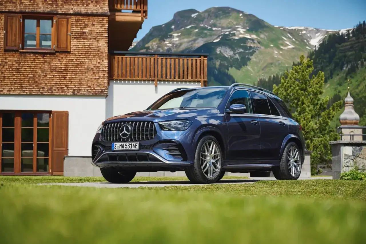 Elegancki, granatowy Mercedes GLE 53 AMG na tle górskiego krajobrazu i drewnianego domu.