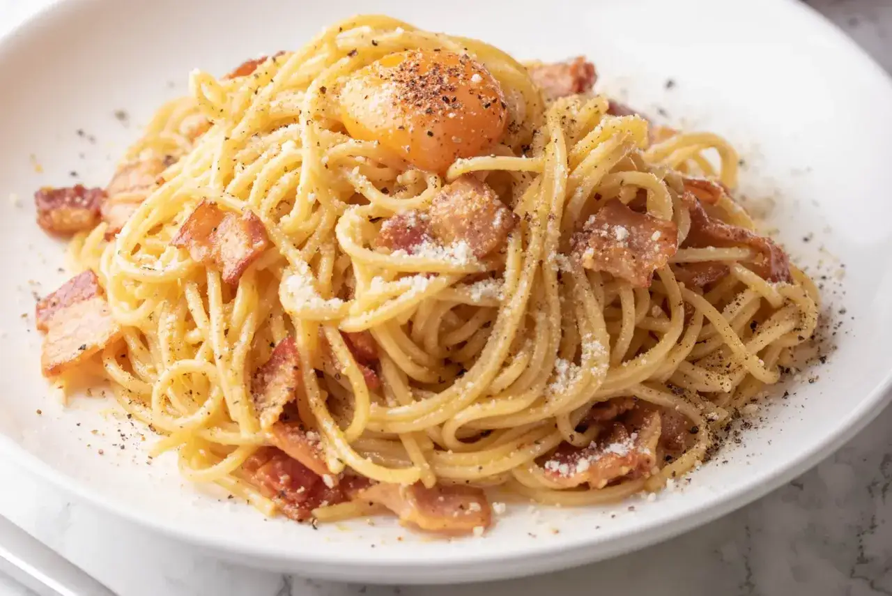 Un plat de spaghetti cr&eacute;meux, garni de lardons croustillants, de parmesan r&acirc;p&eacute;, de poivre noir et d'un jaune d'&oelig;uf coulant, pr&ecirc;t &agrave; &ecirc;tre m&eacute;lang&eacute; pour une sauce carbonara parfaite.