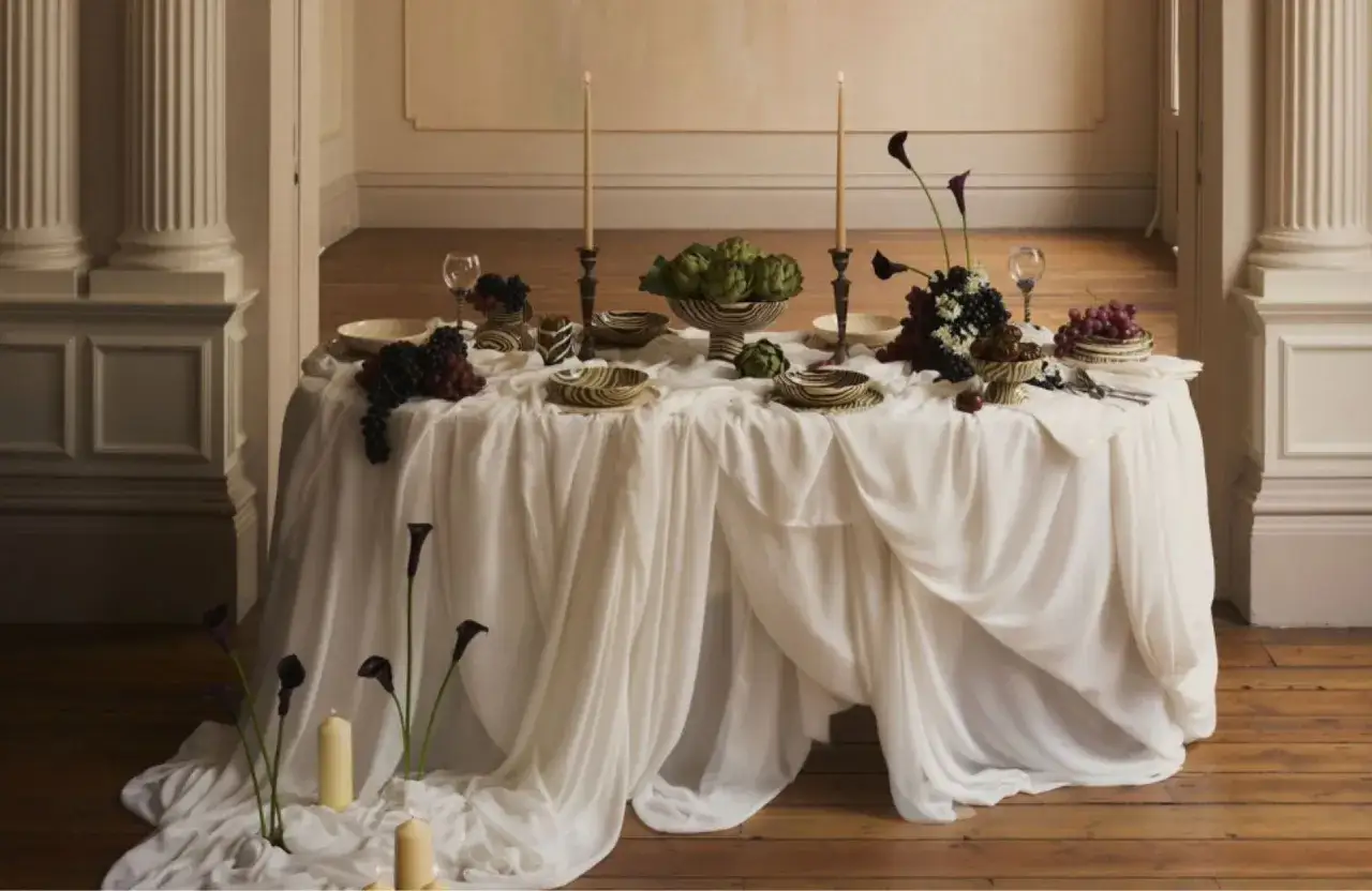 Une table dressée avec élégance, fruits, artichauts et bougies, évoquant l'art de la table française.