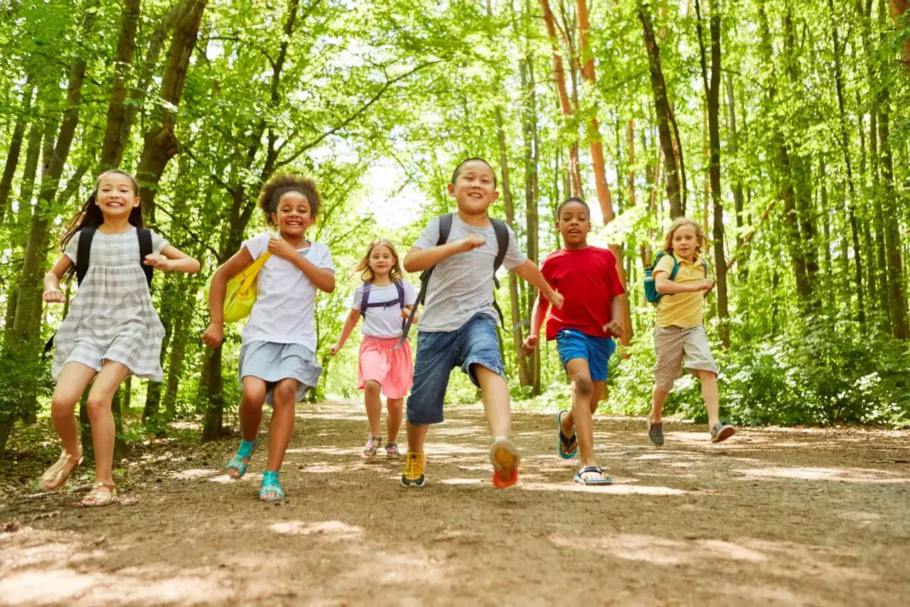 Des enfants courent joyeusement dans une forêt ensoleillée, un avis sur Supernova Juniors.