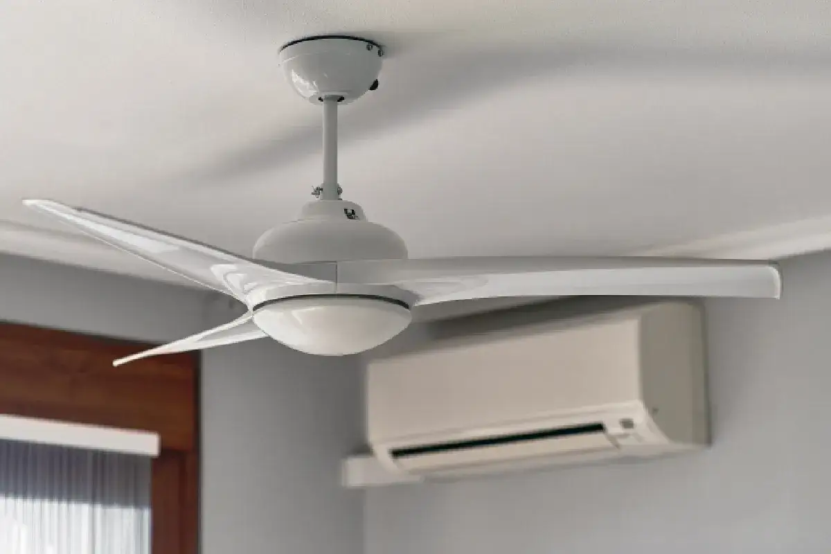 Ventilador de techo blanco moderno con luz, junto a un aire acondicionado. Comprueba si son efectivos los ventiladores de techo para refrescar.