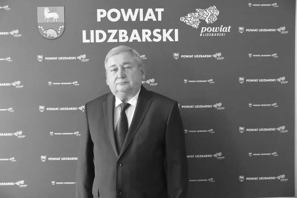 Jan Harhaj, starosta lidzbarski, pozuje na tle ściany z logo powiatu.