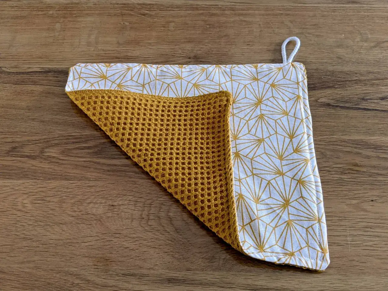 Tuto essuie-tout lavable sans pression : un carré de tissu jaune gaufré et un tissu blanc à motifs géométriques dorés, avec une petite boucle.
