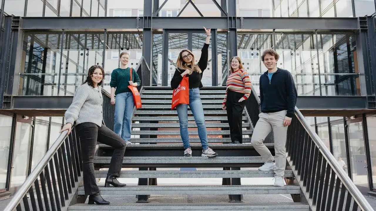 F&uuml;nf junge Leute auf Treppen vor moderner Architektur, bereit f&uuml;r ihr duales Studium Marketing in Berlin.