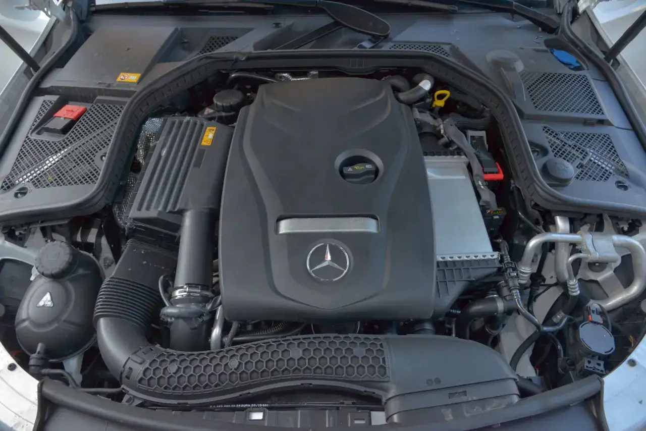 Silnik w mercedes benz klasa c. Widoczny czarny plastikowy wlot powietrza, zbiornik płynu chłodniczego i osłona silnika z logo gwiazdy.