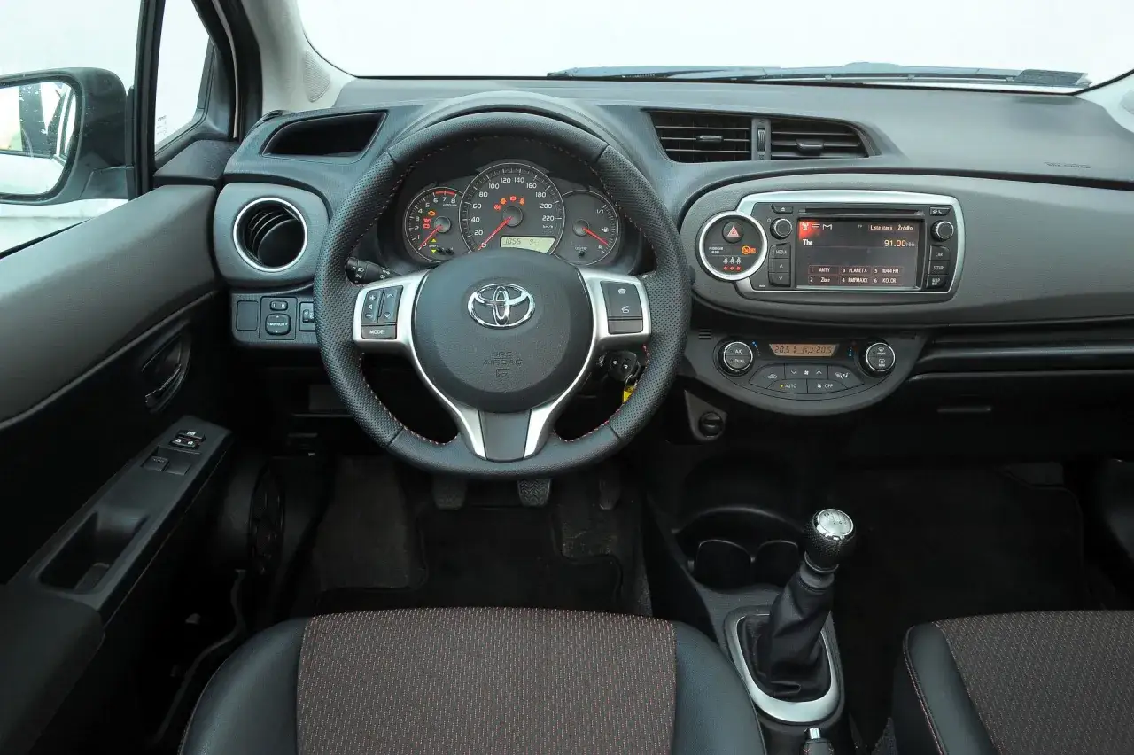 Wnętrze Toyoty Yaris 2008: kierownica, deska rozdzielcza z radiem i nawiewami, dźwignia zmiany biegów.