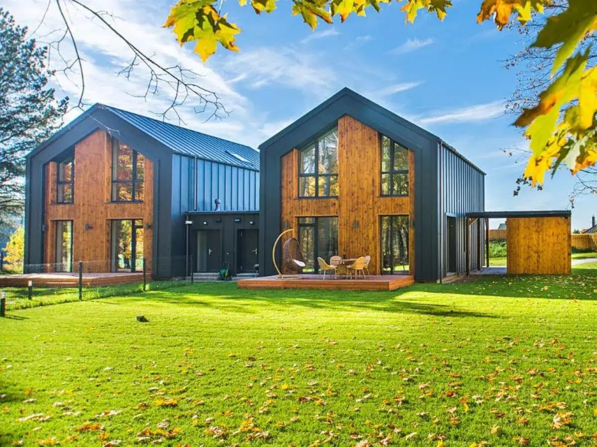 Deux maisons modernes en bois et métal, conçues par un constructeur maison écologique, avec une pelouse verdoyante et des feuilles d'automne.