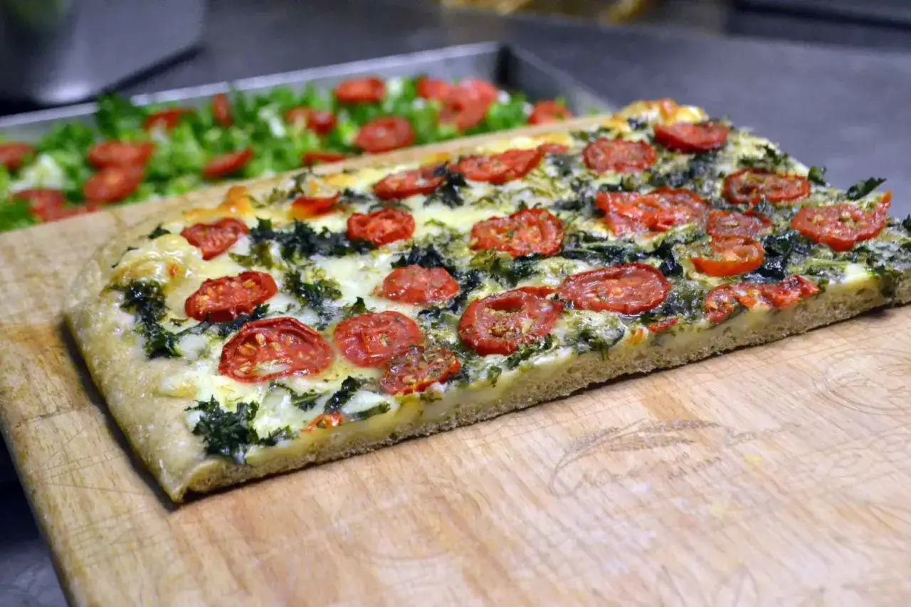 Focaccia messinese con pomodorini e verdure, un piatto invitante su un tagliere di legno.