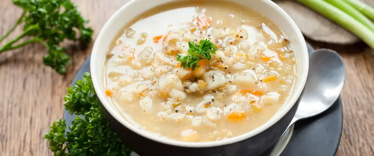 Una ciotola fumante di minestra d'orzo, ricca di verdure e guarnita con prezzemolo fresco, pronta per essere gustata.