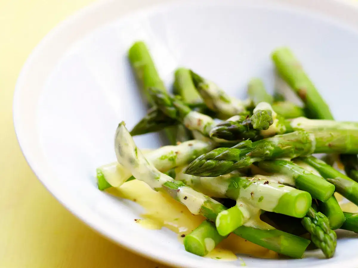 Asperges vertes fra&icirc;ches napp&eacute;es d'une sauce hollandaise l&eacute;g&egrave;re, servies dans une assiette blanche.