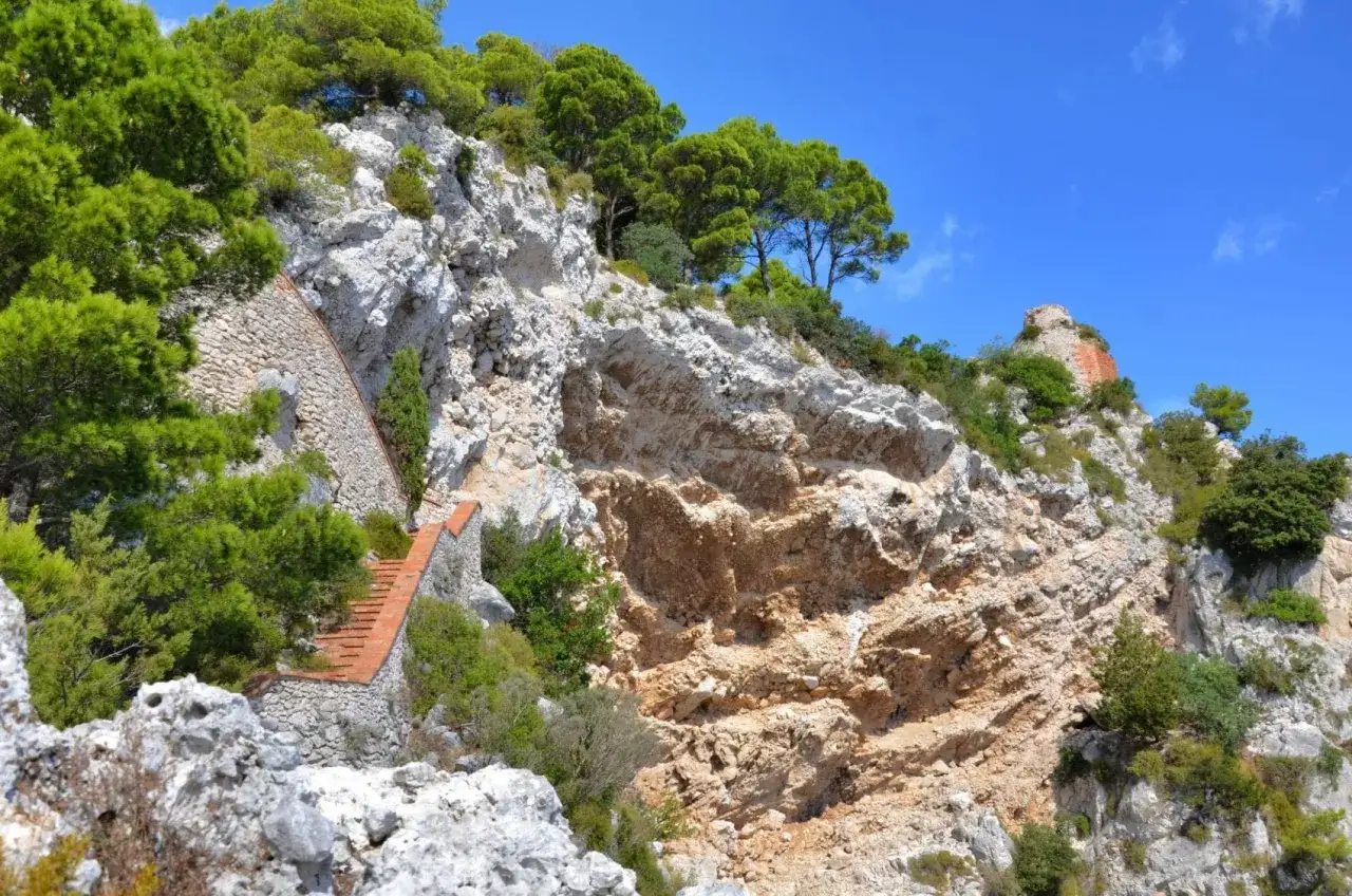 Scogliera rocciosa con vegetazione e una scala in mattoni che sale, evocando il leggendario Salto di Tiberio.