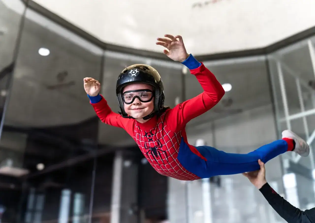 Mały superbohater w stroju Spider-Mana doświadcza ekscytujących lotów w tunelu aerodynamicznym, unosząc się w powietrzu z uśmiechem na twarzy.