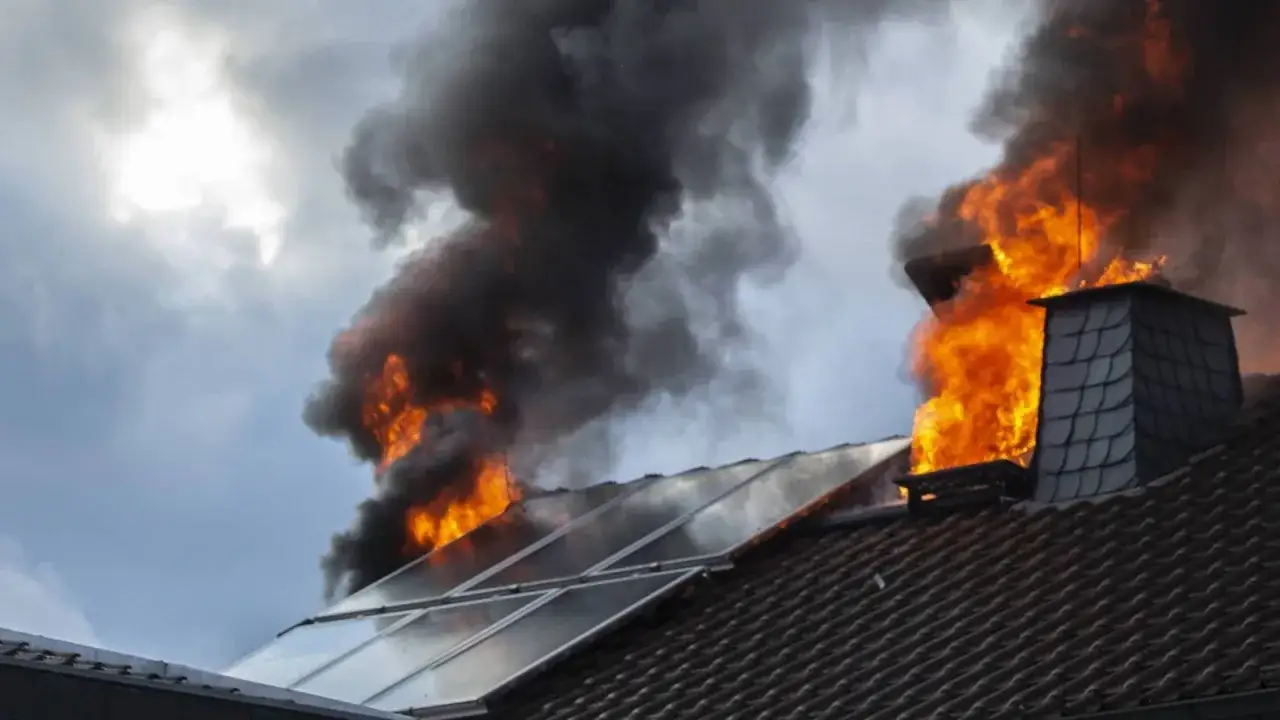Dach mit Photovoltaik-Anlage in Flammen. Dicke schwarze Rauchwolken steigen auf, während Feuer lodert.