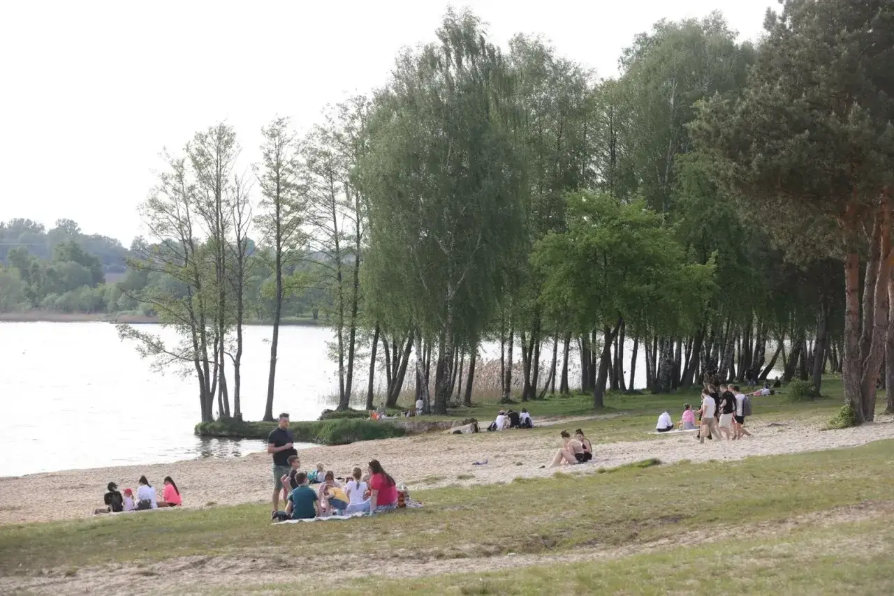 Ludzie odpoczywają na piaszczystej plaży nad jeziorem Pławniowice, ciesząc się wiosennym dniem wśród drzew.
