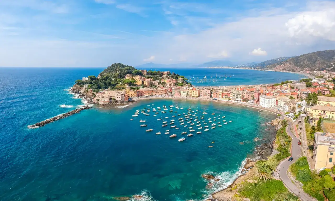 Vue aérienne de la baie de Sestri Levante, avec ses maisons colorées, sa plage et de nombreux bateaux dans les eaux turquoise.