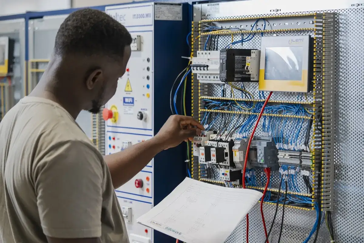 Studente durante corsi per elettricisti, impara a collegare cavi in un quadro elettrico complesso, seguendo uno schema.