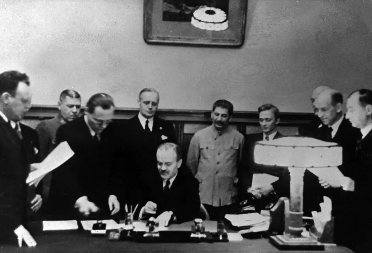 Staline et d'autres hommes en costume signent un document. Le pacte Molotov-Ribbentrop, une alliance entre l'URSS et l'Allemagne nazie, est signé.