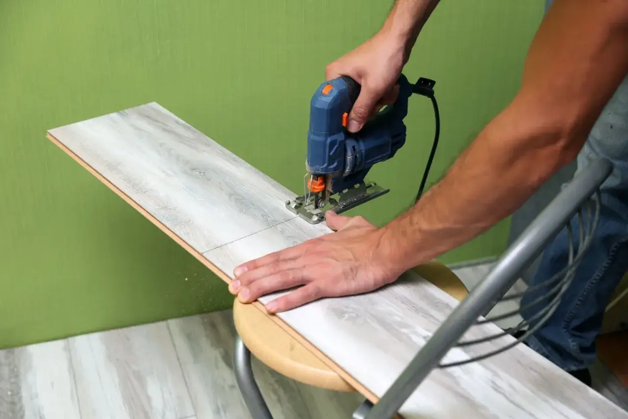Un homme utilise une scie sauteuse pour découper une lame de parquet stratifié.