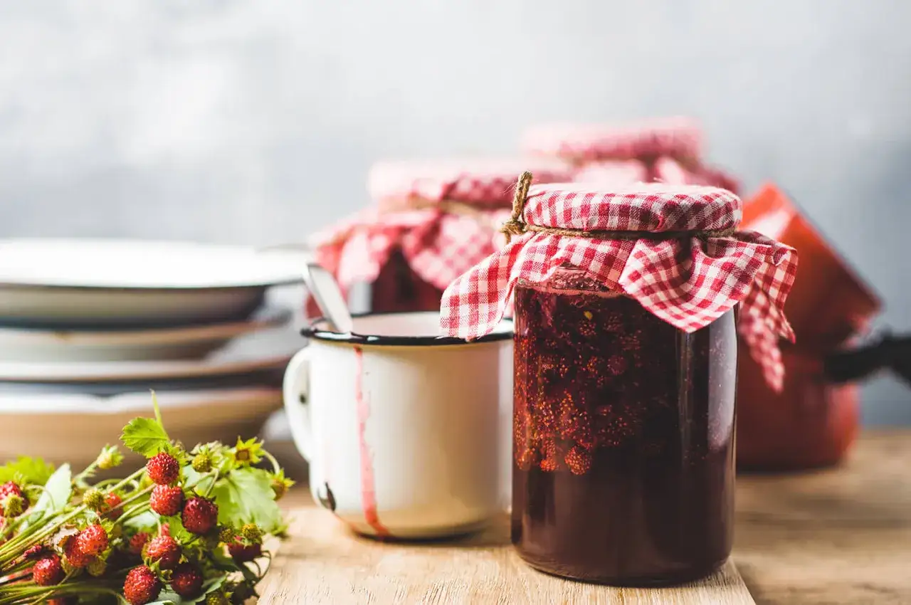 Gl&auml;ser mit Erdbeermarmelade, bereit zum Marmelade einfrieren. Ein Becher und frische Erdbeeren liegen daneben.