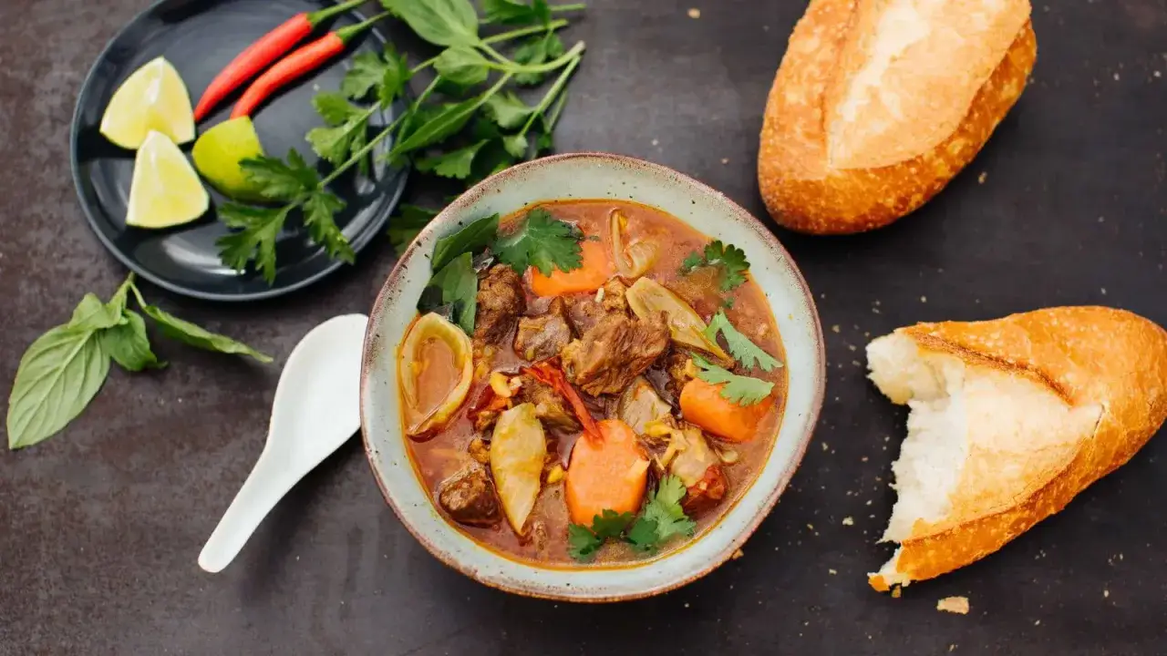 Herzhaftes Bo Kho, ein vietnamesischer Rindfleischeintopf mit Karotten und Kr&auml;utern, serviert mit Baguette.