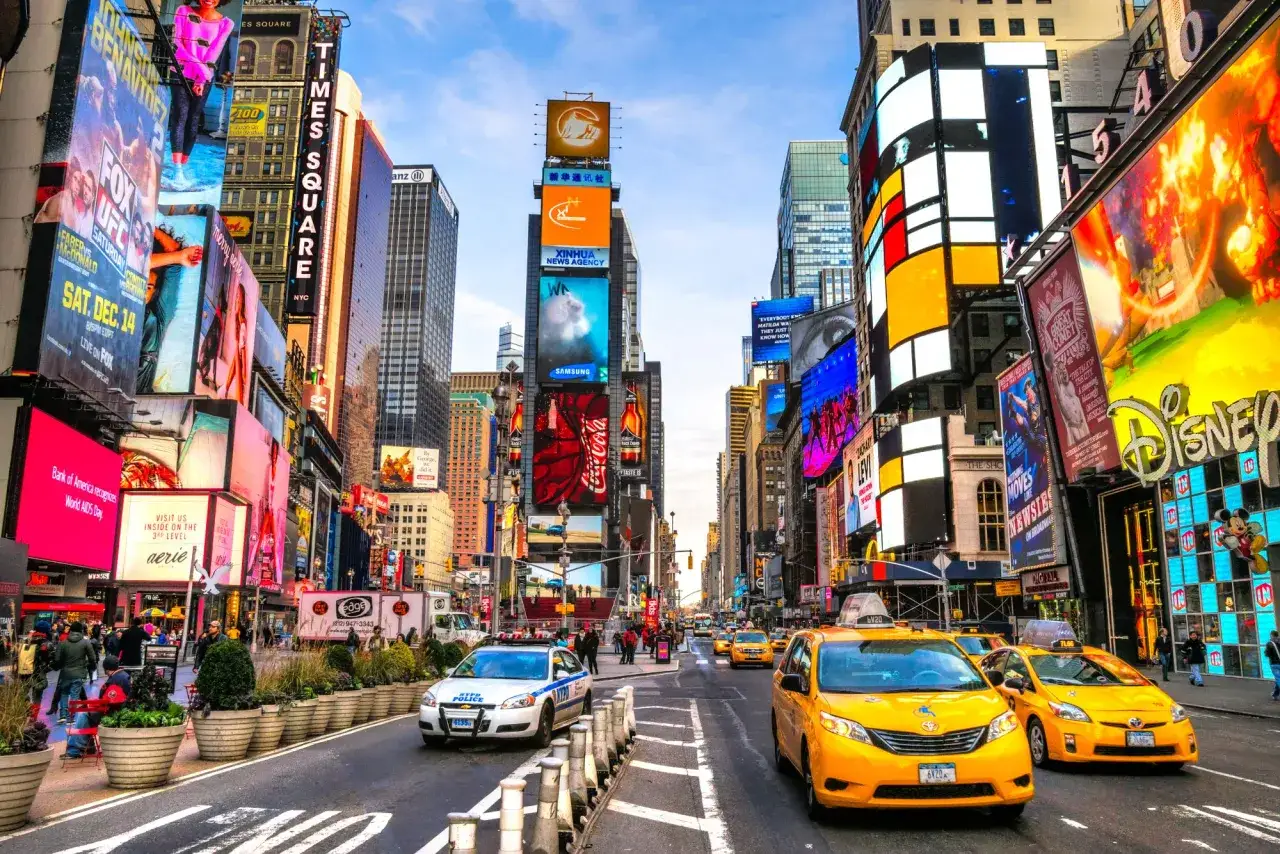 Jasne, oto propozycja:
Tłumy ludzi i żółte taksówki na Times Square w Nowym Jorku. Zastanawiasz się, ile kosztuje lot do Stanów Zjednoczonych?