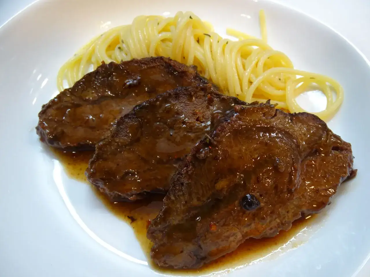 Tres tiernas carrilleras al vino tinto, ba&ntilde;adas en su salsa, acompa&ntilde;adas de espaguetis.