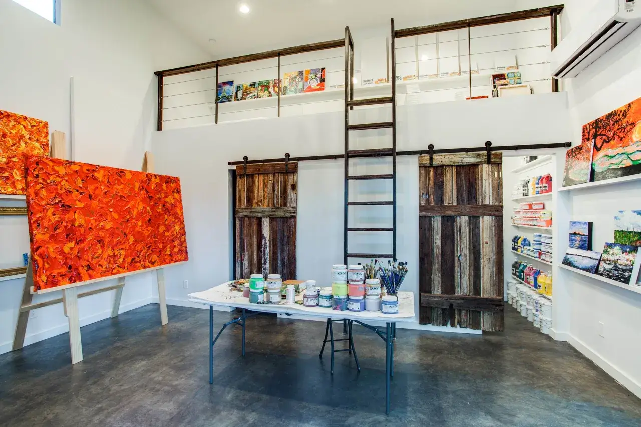 Atelier d'un artiste peintre auto entrepreneur : toiles vibrantes, pots de peinture, chevalets et portes coulissantes rustiques.