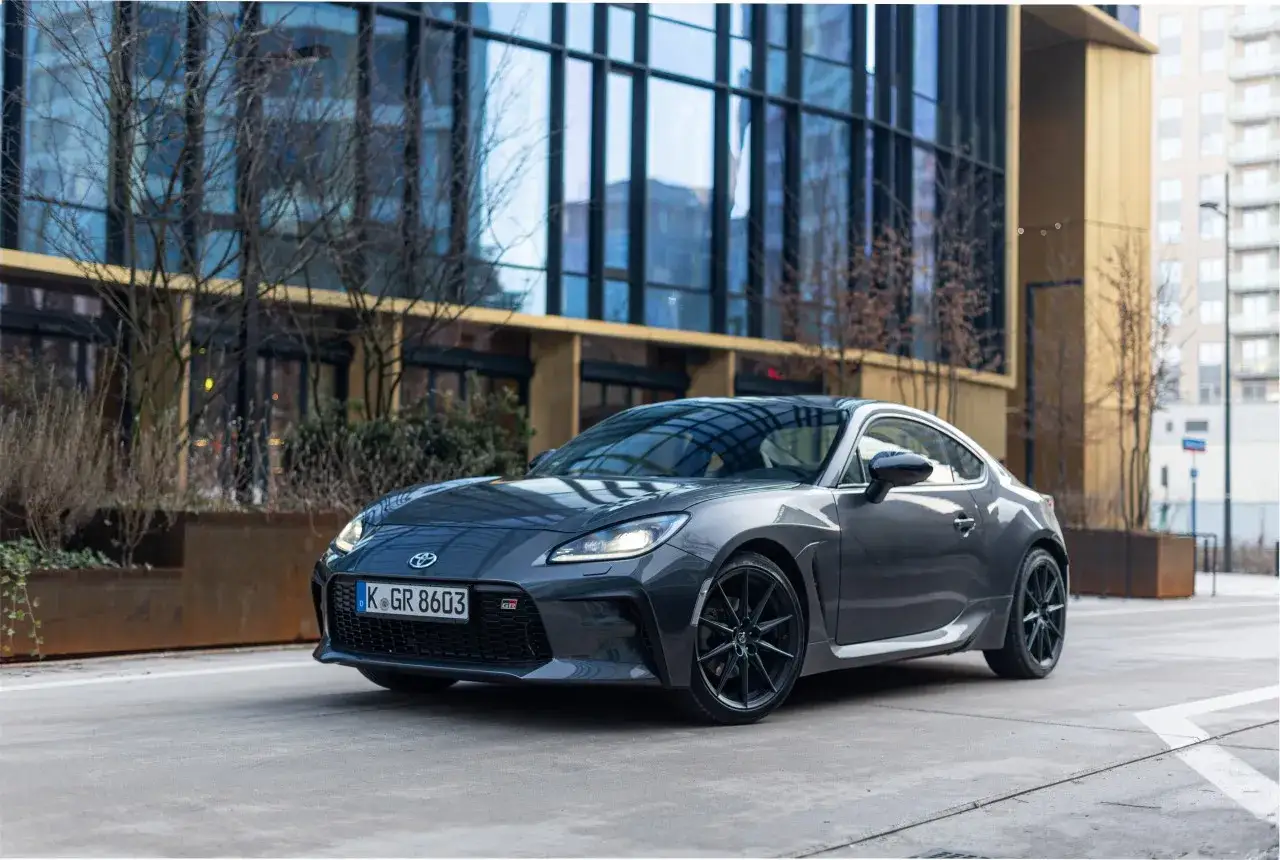 Szary Toyota 86 z czarnymi felgami stoi przed nowoczesnym budynkiem.