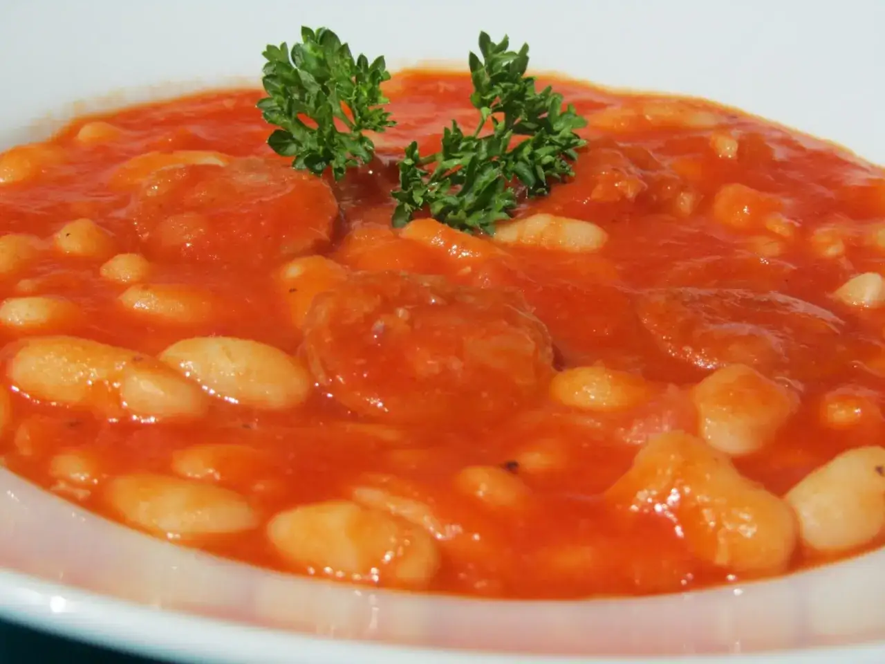 Un plato de pochas a la navarra, con jud&iacute;as blancas tiernas en una salsa de tomate rojiza y trozos de chorizo, decorado con perejil fresco.