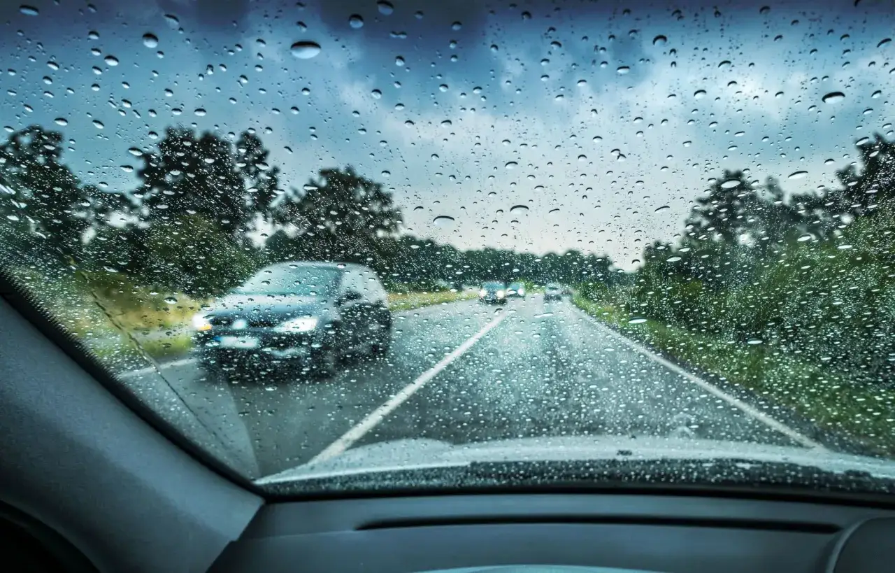 Si conduciendo le sorprende una lluvia torrencial, el parabrisas se llena de gotas. La carretera se ve mojada y otros coches circulan con precaución.