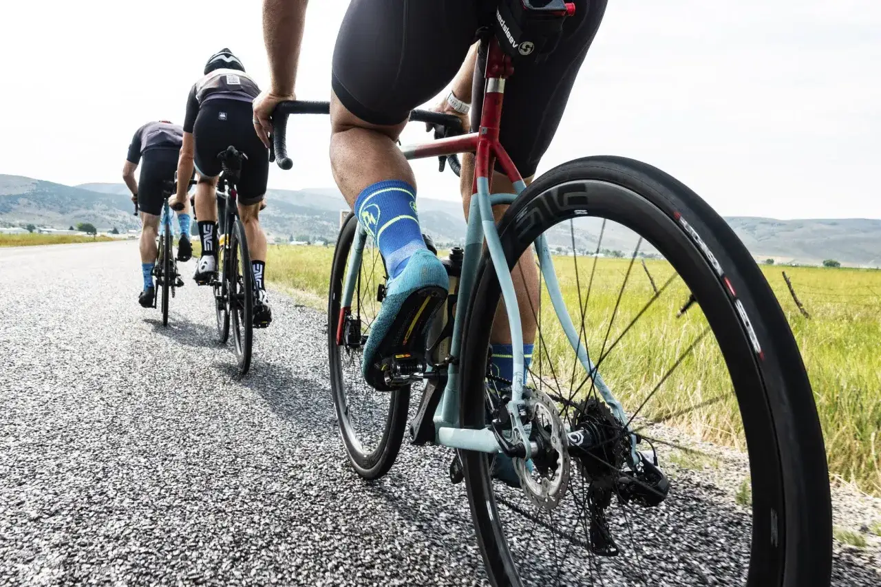 Cyclists on an endurance bike vs road bike race down a gravel road, legs pumping, with mountains in the distance.
