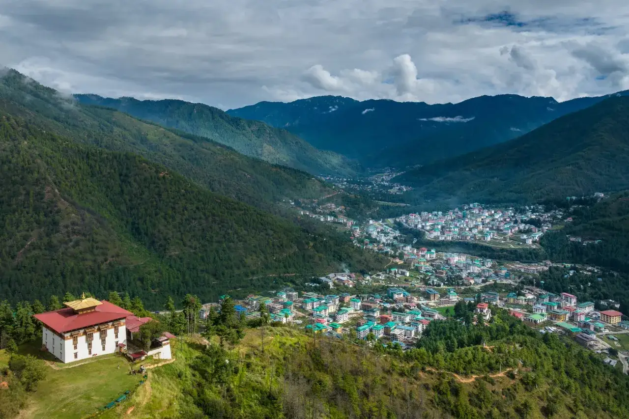 Malowniczy krajobraz Bhutan z klasztorem na wzgórzu i miastem w dolinie. Taka wycieczka to marzenie, a cena może być zaskakująco przystępna.