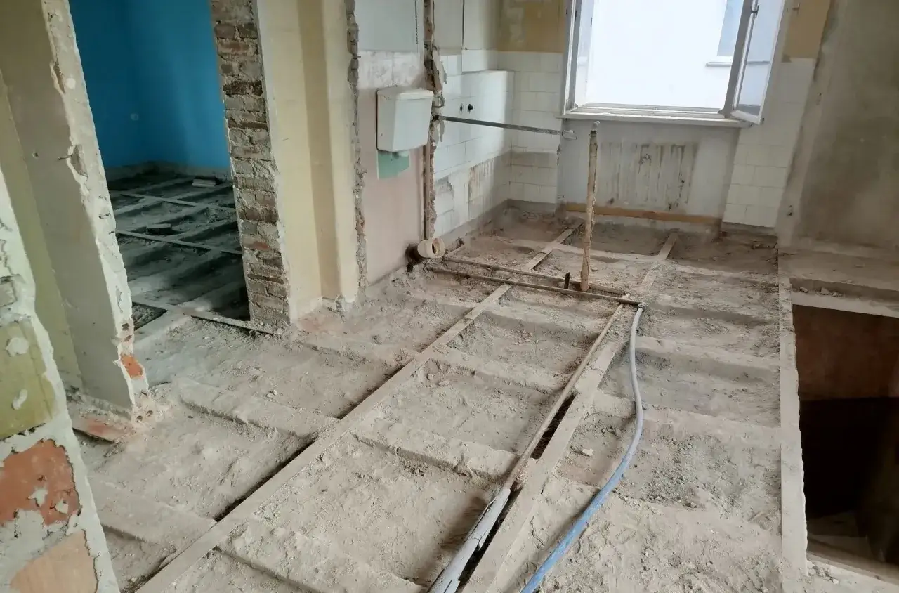 Remontowane wnętrze z odsłoniętą podłogą, ceglanymi ścianami i instalacjami.