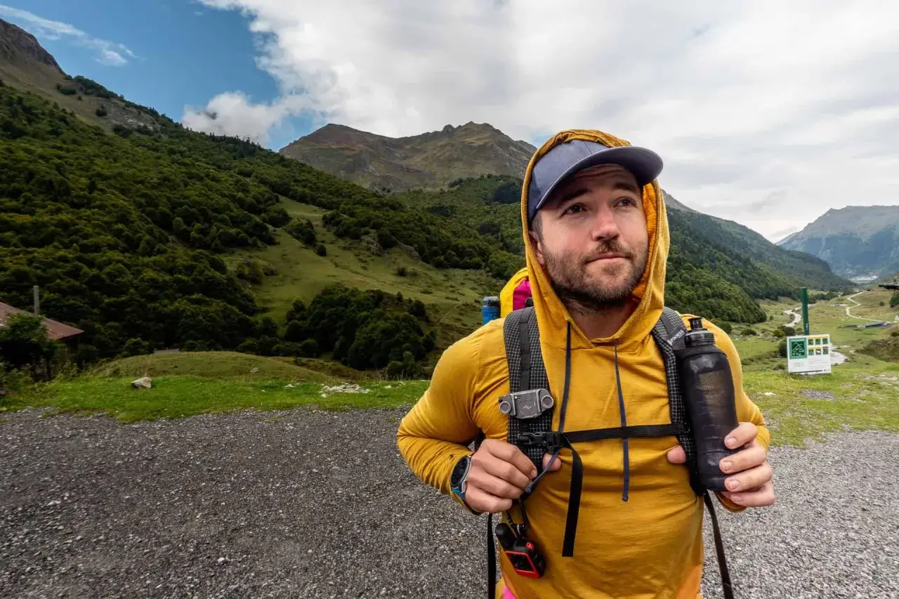 Mann mit Rucksack und Trinkflasche im Gebirge, bereit für Speed Hiking.