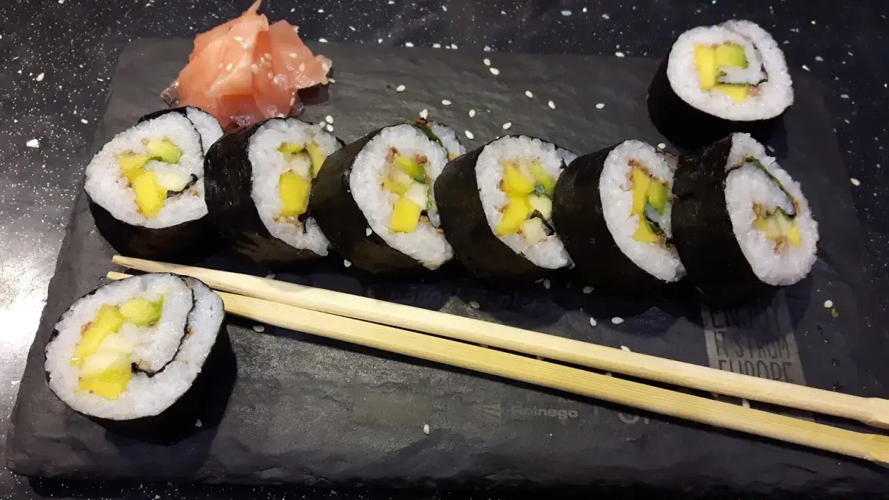 Słodkie sushi z mango i awokado, podane z imbirem na czarnej desce.