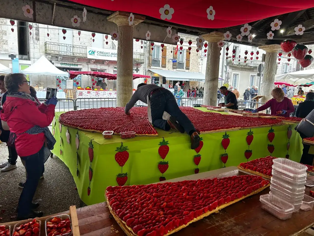 Une immense tarte aux fraises est préparée pour la fête de la fraise. Des décorations de fraises et de fleurs ornent l'espace.