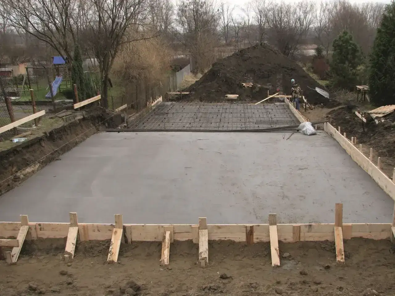 Plac budowy z wylana płytą betonową, zbrojeniem i szalunkiem. Powstają fundamenty, przyszłe klasy betonu czekają na dalsze prace.