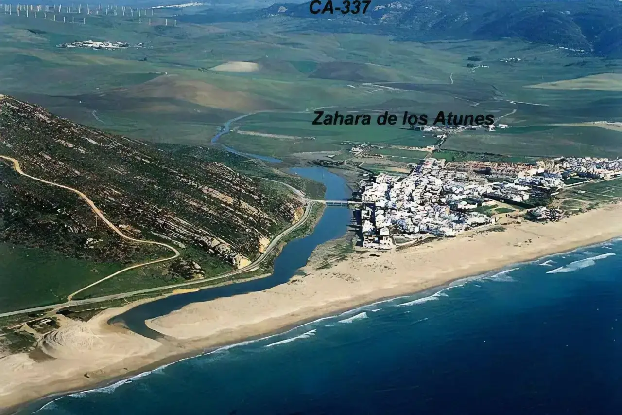 Vista aérea del pueblo y paseo marítimo de Zahara de los Atunes, con su playa, el río y colinas verdes.