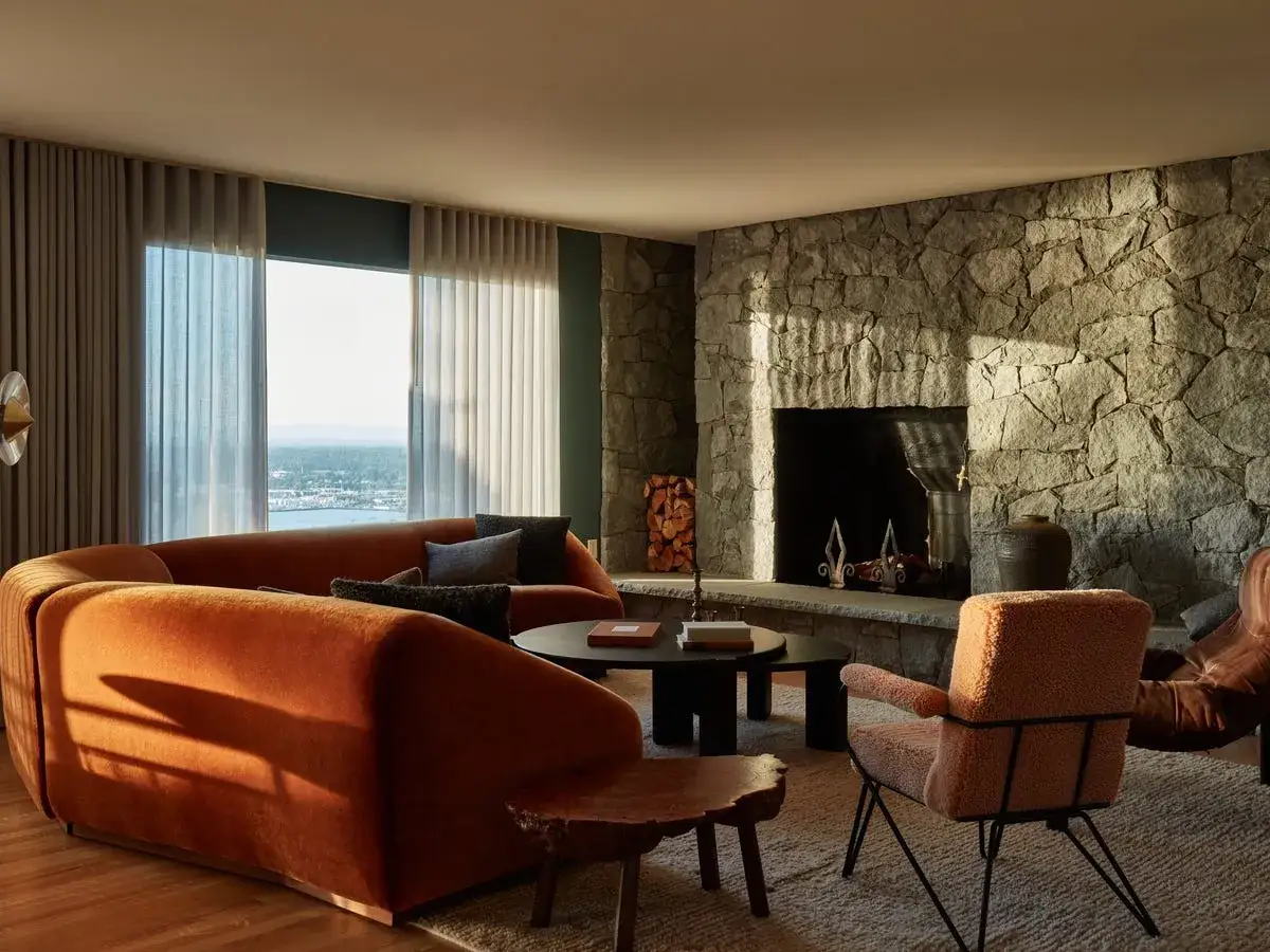Sof&aacute; curvo naranja y sill&oacute;n de borrego, con chimenea de piedra y ventana al mar. Un ambiente con un toque de dise&ntilde;o a&ntilde;os 50.