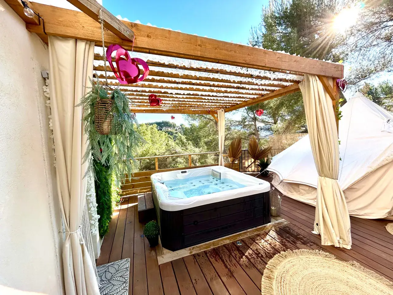 Jacuzzi extérieur sous pergola, décoré de cœurs roses, avec une yourte dans les Alpes-Maritimes. Ambiance romantique et détente assurée.