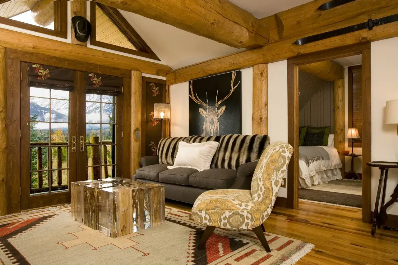Salon rustique avec tableau de cerf, une excellente id&eacute;e d&eacute;co avec bois de cerf. Canap&eacute; confortable, table basse en bois et verre, et vue sur les montagnes.