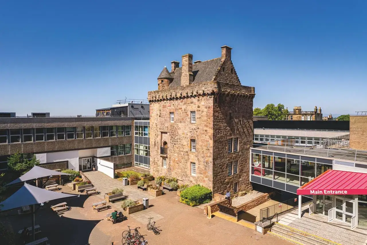 Historischer Turm auf dem Campus der Edinburgh Napier University, umgeben von modernen Gebäuden und einem Innenhof mit Sitzgelegenheiten.