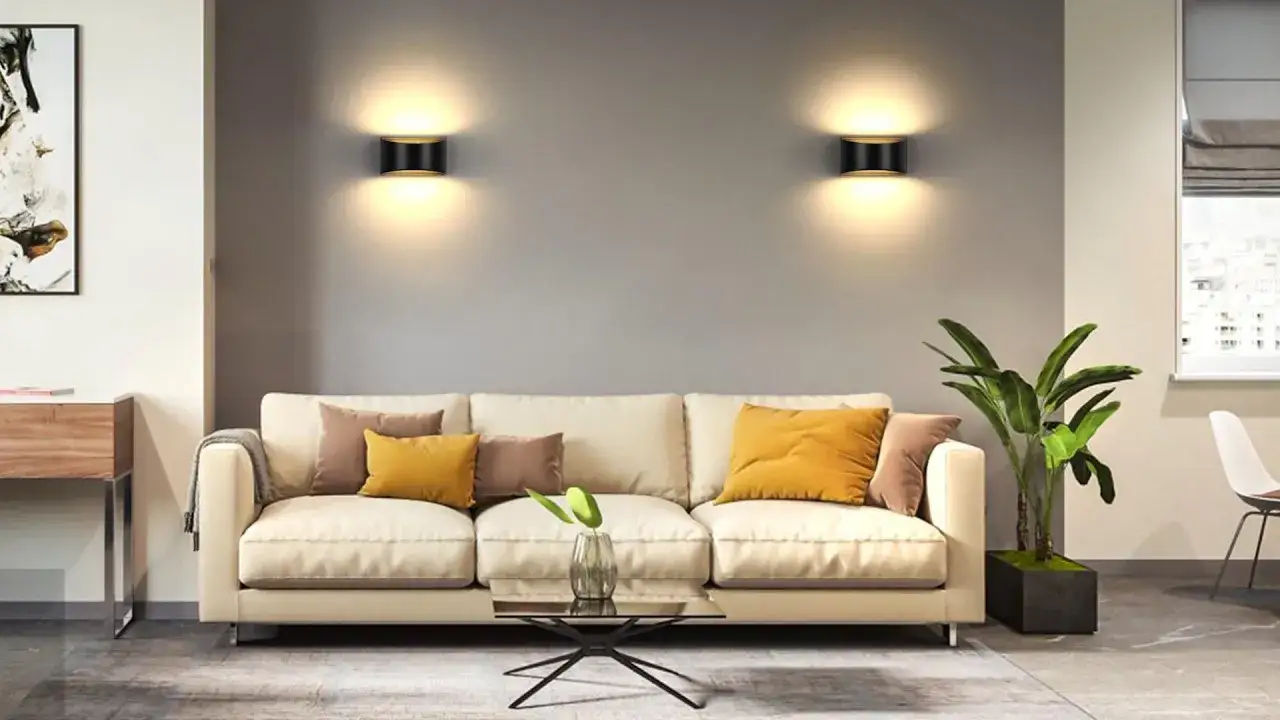 Dos apliques pared regulable negros con detalles dorados iluminan un salón moderno con sofá beige y cojines amarillos y marrones.